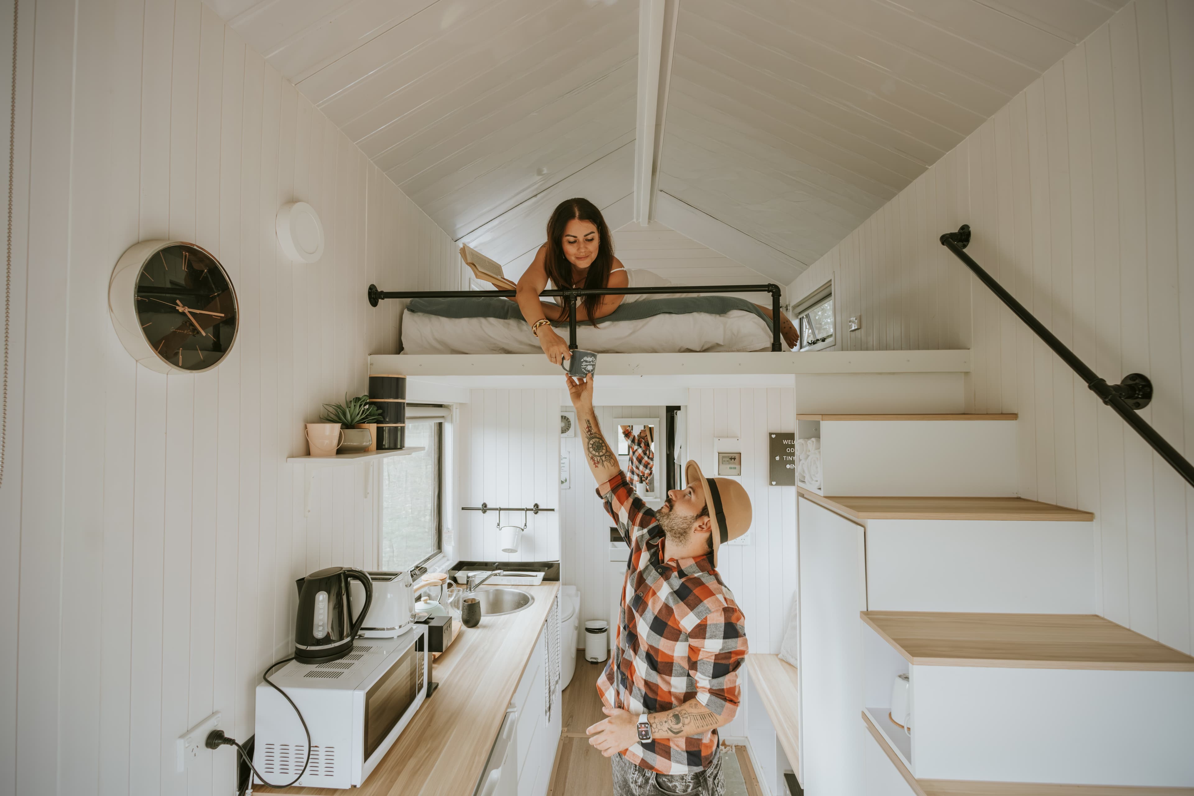 Man hands a mug to a woman in a loft bed inside a tiny home.
