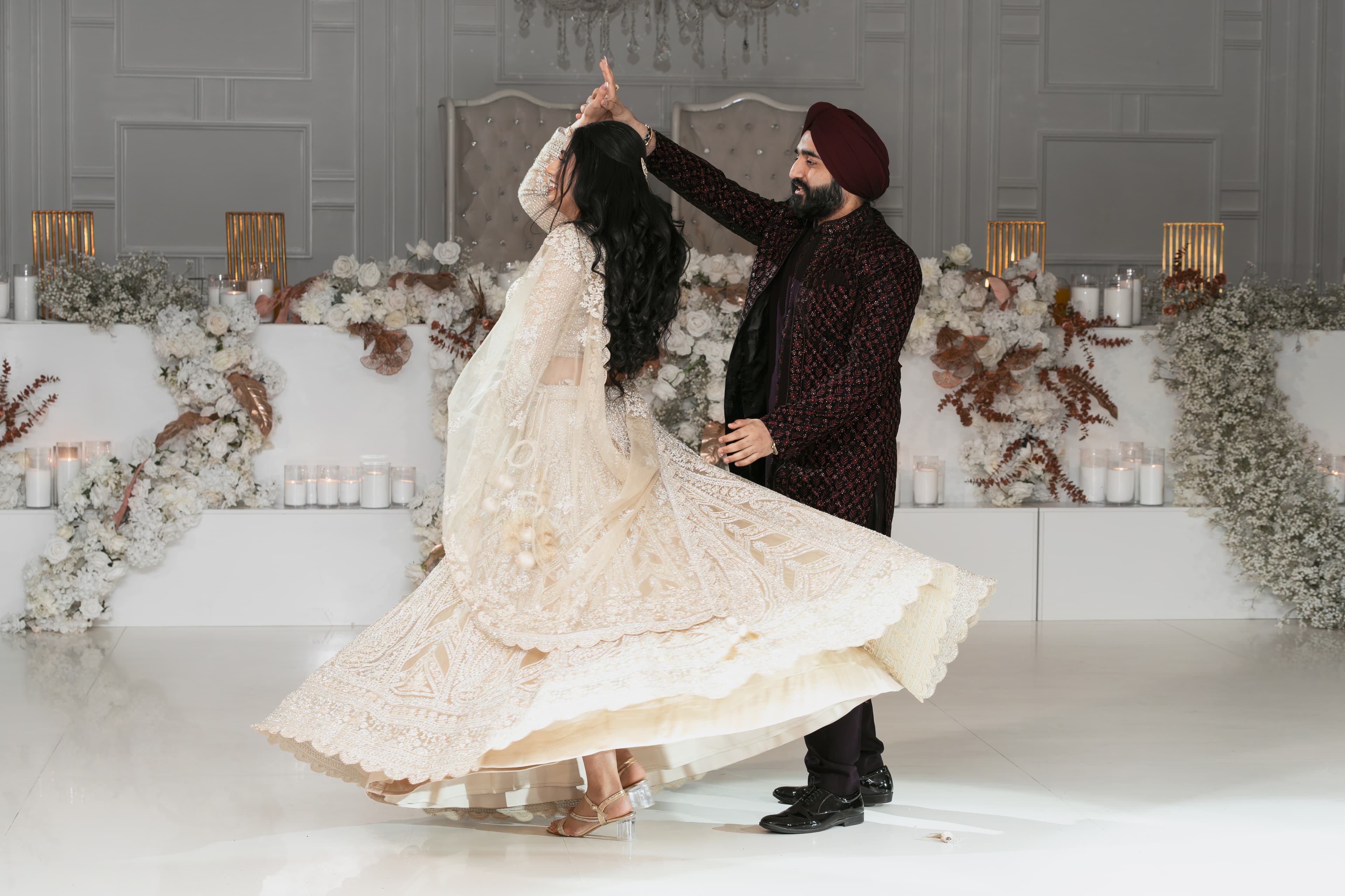 A Sikh groom in a maroon sherwani spins his bride in a white lehenga.
