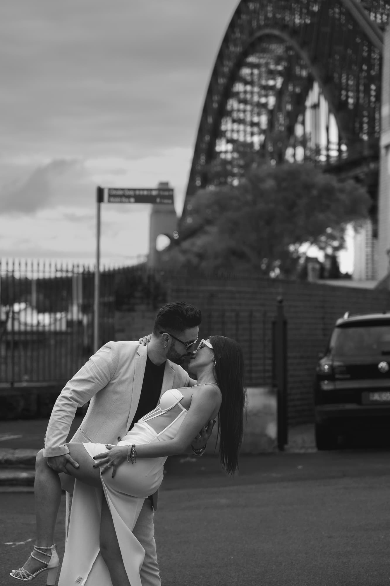 Man in suit dips and kisses woman in white dress near the Sydney Harbour Bridge.