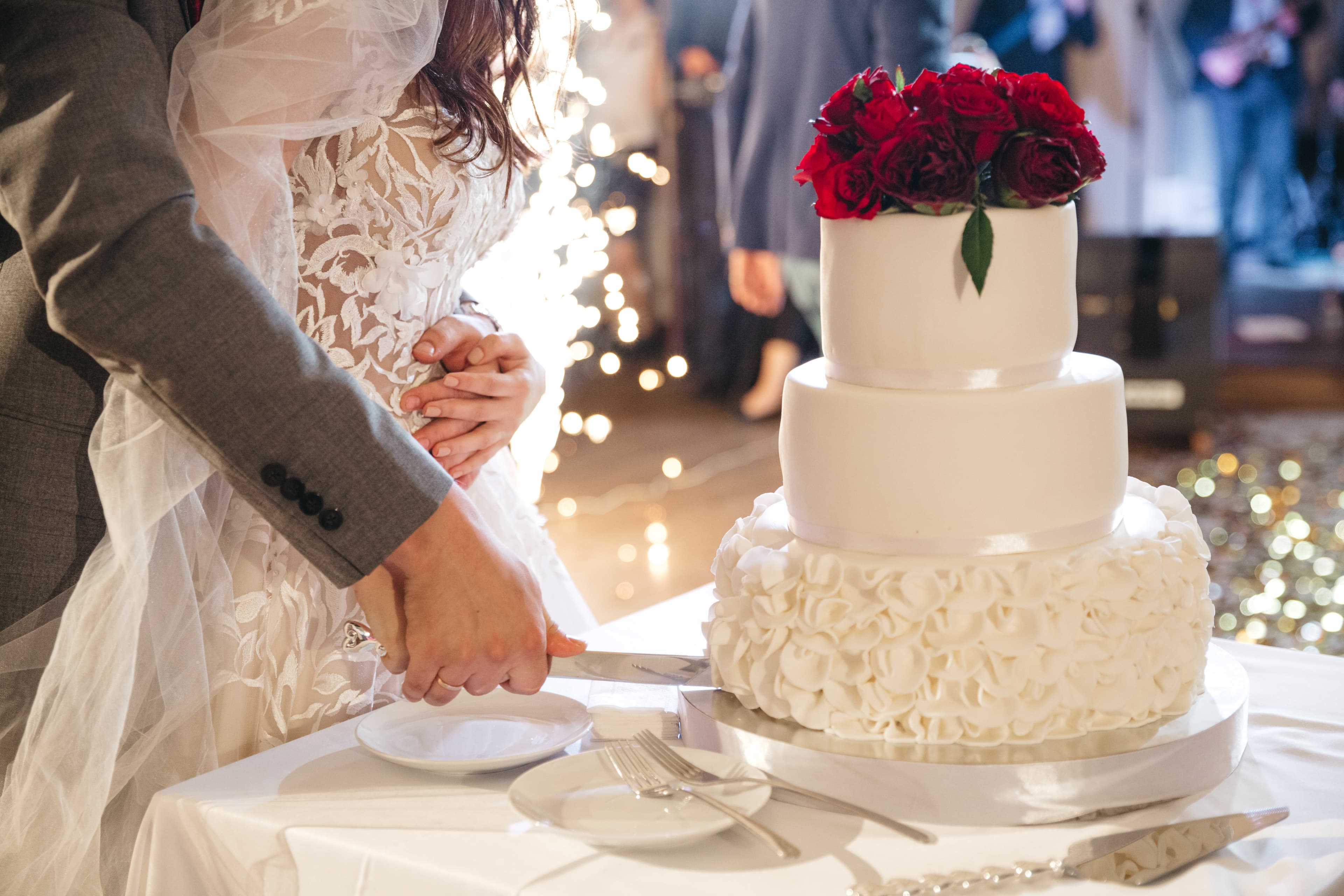 A bride and groom cutting a white three-tiered wedding cake topped with red roses.
