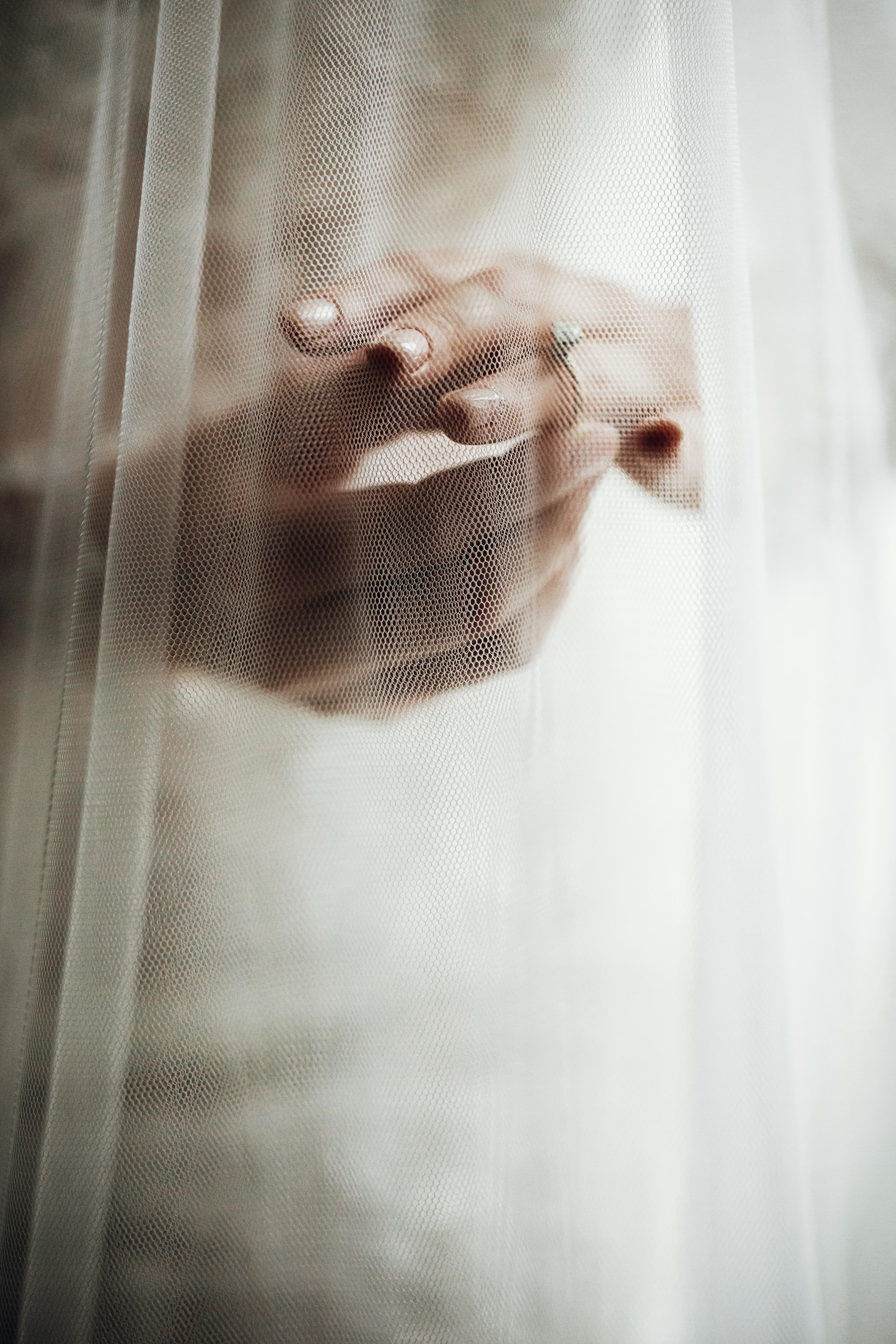A bride's hands with a diamond ring visible through a sheer white wedding veil.